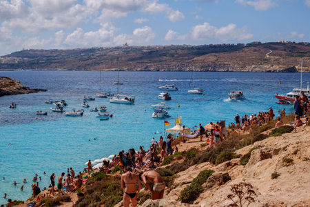 Comino, Malta - July 18, 2019. Tourists crowd at Blue Lagoon to enjoy the clear turquoise water on a sunny summer day with and boats on Comino island, Malta.のeditorial素材
