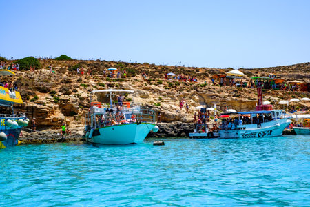 Comino, Malta - July 23, 2019. Tourists crowd at Blue Lagoon to enjoy the clear turquoise water on a sunny summer day with boats on Comino island, Malta.のeditorial素材