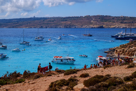 Comino, Malta - July 18, 2019. Tourists crowd at Blue Lagoon to enjoy the clear turquoise water on a sunny summer day with and boats on Comino island, Malta.のeditorial素材