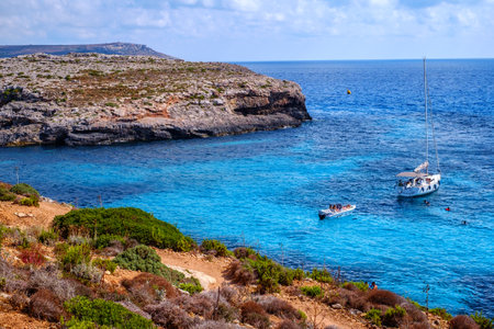 Comino, Malta - July 18, 2019. Tourists crowd at Blue Lagoon to enjoy the clear turquoise water on a sunny summer day with and boats on Comino island, Malta.のeditorial素材