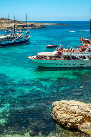 Comino, Malta - July 23, 2019. Tourists crowd at Blue Lagoon to enjoy the clear turquoise water on a sunny summer day with boats on Comino island, Malta.のeditorial素材
