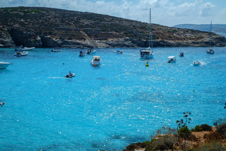 Comino, Malta - July 18, 2019. Tourists crowd at Blue Lagoon to enjoy the clear turquoise water on a sunny summer day with and boats on Comino island, Malta.のeditorial素材