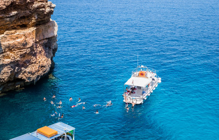 Comino, Malta - July 23, 2019. Tourists crowd at Blue Lagoon to enjoy the clear turquoise water on a sunny summer day with boats on Comino island, Malta.のeditorial素材