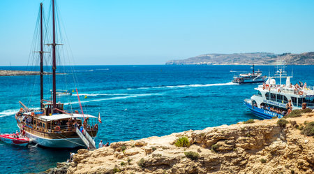 Comino, Malta - July 23, 2019. Tourists crowd at Blue Lagoon to enjoy the clear turquoise water on a sunny summer day with boats on Comino island, Malta.のeditorial素材