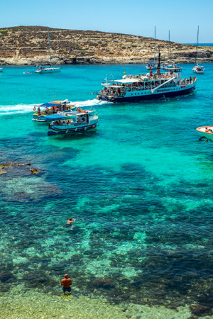 Comino, Malta - July 23, 2019. Tourists crowd at Blue Lagoon to enjoy the clear turquoise water on a sunny summer day with boats on Comino island, Malta.のeditorial素材