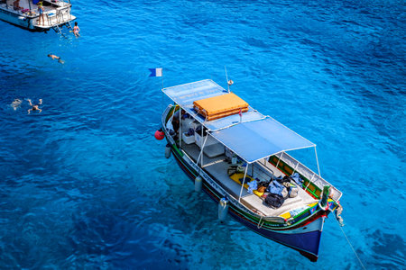 Comino, Malta - July 23, 2019. Tourists crowd at Blue Lagoon to enjoy the clear turquoise water on a sunny summer day with boats on Comino island, Malta.のeditorial素材