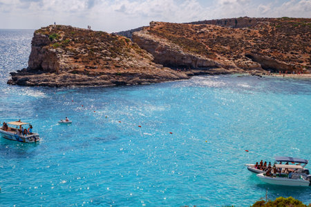 Comino, Malta - July 18, 2019. Tourists crowd at Blue Lagoon to enjoy the clear turquoise water on a sunny summer day with and boats on Comino island, Malta.のeditorial素材