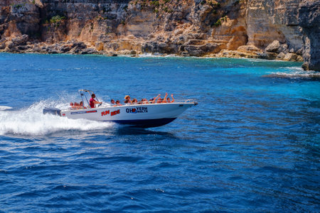 Comino, Malta - July 18, 2019. Tourists crowd at Blue Lagoon to enjoy the clear turquoise water on a sunny summer day with and boats on Comino island, Malta.のeditorial素材