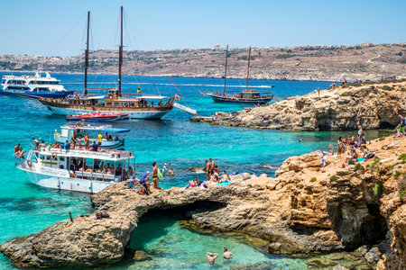 Comino, Malta - July 23, 2019. Tourists crowd at Blue Lagoon to enjoy the clear turquoise water on a sunny summer day with boats on Comino island, Malta.のeditorial素材
