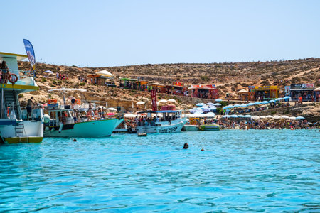Comino, Malta - July 23, 2019. Tourists crowd at Blue Lagoon to enjoy the clear turquoise water on a sunny summer day with boats on Comino island, Malta.のeditorial素材