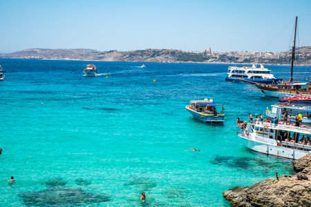 Comino, Malta - July 23, 2019. Tourists crowd at Blue Lagoon to enjoy the clear turquoise water on a sunny summer day with boats on Comino island, Malta.のeditorial素材