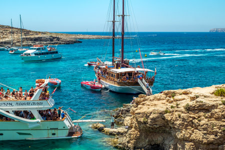 Comino, Malta - July 23, 2019. Tourists crowd at Blue Lagoon to enjoy the clear turquoise water on a sunny summer day with boats on Comino island, Malta.のeditorial素材