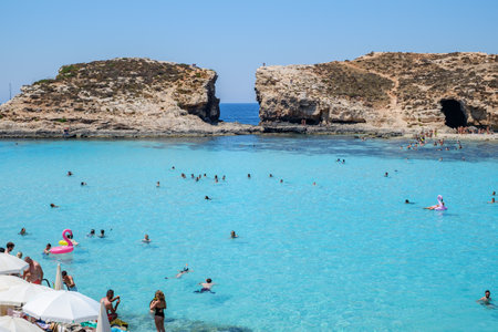 Comino, Malta - July 23, 2019. Tourists crowd at Blue Lagoon to enjoy the clear turquoise water on a sunny summer day with boats on Comino island, Malta.のeditorial素材