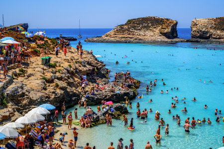 Comino, Malta - July 23, 2019. Tourists crowd at Blue Lagoon to enjoy the clear turquoise water on a sunny summer day with boats on Comino island, Malta.のeditorial素材