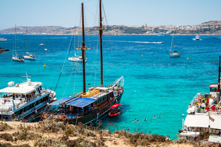 Comino, Malta - July 23, 2019. Tourists crowd at Blue Lagoon to enjoy the clear turquoise water on a sunny summer day with boats on Comino island, Malta.のeditorial素材