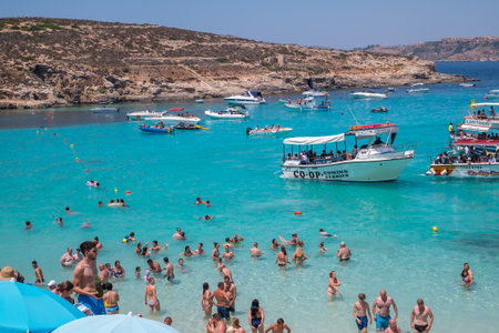 Comino, Malta - July 23, 2019. Tourists crowd at Blue Lagoon to enjoy the clear turquoise water on a sunny summer day with boats on Comino island, Malta.のeditorial素材