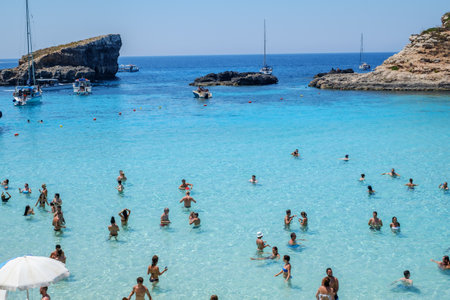 Comino, Malta - July 23, 2019. Tourists crowd at Blue Lagoon to enjoy the clear turquoise water on a sunny summer day with boats on Comino island, Malta.のeditorial素材