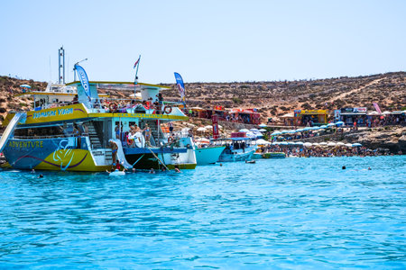 Comino, Malta - July 23, 2019. Tourists crowd at Blue Lagoon to enjoy the clear turquoise water on a sunny summer day with boats on Comino island, Malta.のeditorial素材