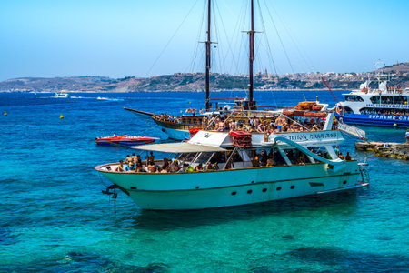 Comino, Malta - July 23, 2019. Tourists crowd at Blue Lagoon to enjoy the clear turquoise water on a sunny summer day with boats on Comino island, Malta.のeditorial素材