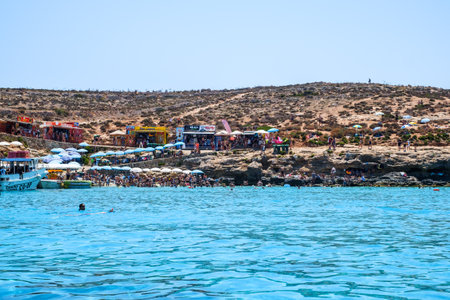 Comino, Malta - July 23, 2019. Tourists crowd at Blue Lagoon to enjoy the clear turquoise water on a sunny summer day with boats on Comino island, Malta.のeditorial素材