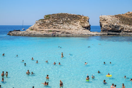 Comino, Malta - July 23, 2019. Tourists crowd at Blue Lagoon to enjoy the clear turquoise water on a sunny summer day with boats on Comino island, Malta.のeditorial素材