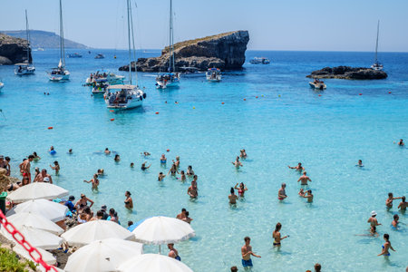 Comino, Malta - July 23, 2019. Tourists crowd at Blue Lagoon to enjoy the clear turquoise water on a sunny summer day with boats on Comino island, Malta.のeditorial素材
