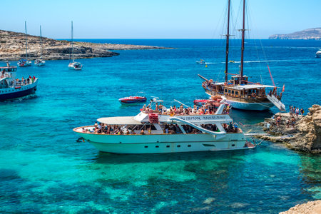 Comino, Malta - July 23, 2019. Tourists crowd at Blue Lagoon to enjoy the clear turquoise water on a sunny summer day with boats on Comino island, Malta.のeditorial素材