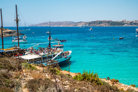 Comino, Malta - July 23, 2019. Tourists crowd at Blue Lagoon to enjoy the clear turquoise water on a sunny summer day with boats on Comino island, Malta.のeditorial素材