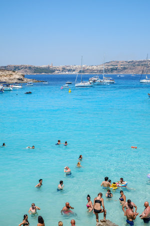 Comino, Malta - July 23, 2019. Tourists crowd at Blue Lagoon to enjoy the clear turquoise water on a sunny summer day with boats on Comino island, Malta.のeditorial素材