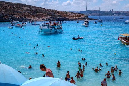 Comino, Malta - July 18, 2019. Tourists crowd at Blue Lagoon to enjoy the clear turquoise water on a sunny summer day with and boats on Comino island, Malta.のeditorial素材