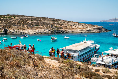 Comino, Malta - July 23, 2019. Tourists crowd at Blue Lagoon to enjoy the clear turquoise water on a sunny summer day with boats on Comino island, Malta.のeditorial素材