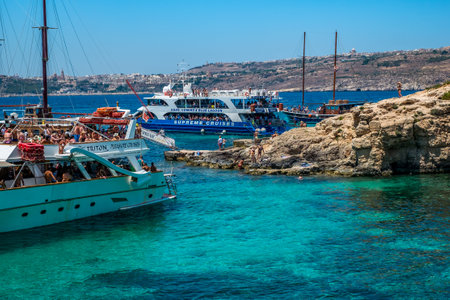 Comino, Malta - July 23, 2019. Tourists crowd at Blue Lagoon to enjoy the clear turquoise water on a sunny summer day with boats on Comino island, Malta.のeditorial素材