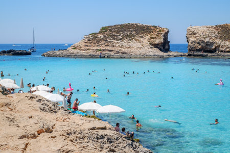 Comino, Malta - July 23, 2019. Tourists crowd at Blue Lagoon to enjoy the clear turquoise water on a sunny summer day with boats on Comino island, Malta.のeditorial素材