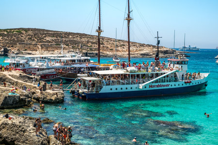 Comino, Malta - July 23, 2019. Tourists crowd at Blue Lagoon to enjoy the clear turquoise water on a sunny summer day with boats on Comino island, Malta.のeditorial素材