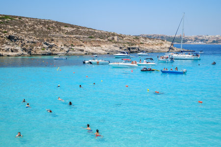 Comino, Malta - July 23, 2019. Tourists crowd at Blue Lagoon to enjoy the clear turquoise water on a sunny summer day with boats on Comino island, Malta.のeditorial素材