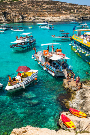 Comino, Malta - July 23, 2019. Tourists crowd at Blue Lagoon to enjoy the clear turquoise water on a sunny summer day with boats on Comino island, Malta.のeditorial素材