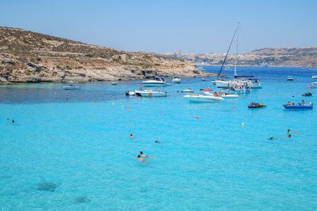 Comino, Malta - July 23, 2019. Tourists crowd at Blue Lagoon to enjoy the clear turquoise water on a sunny summer day with boats on Comino island, Malta.のeditorial素材