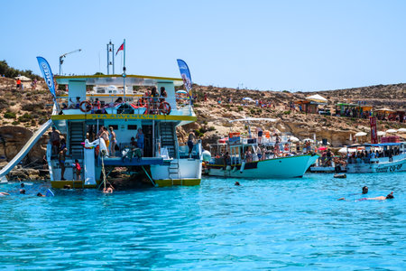 Comino, Malta - July 23, 2019. Tourists crowd at Blue Lagoon to enjoy the clear turquoise water on a sunny summer day with boats on Comino island, Malta.のeditorial素材