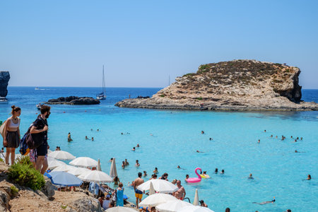 Comino, Malta - July 23, 2019. Tourists crowd at Blue Lagoon to enjoy the clear turquoise water on a sunny summer day with boats on Comino island, Malta.のeditorial素材