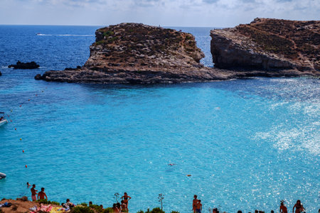 Comino, Malta - July 18, 2019. Tourists crowd at Blue Lagoon to enjoy the clear turquoise water on a sunny summer day with and boats on Comino island, Malta.のeditorial素材