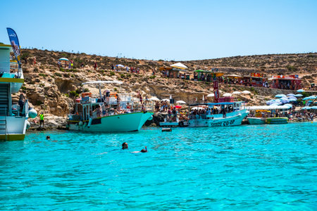 Comino, Malta - July 23, 2019. Tourists crowd at Blue Lagoon to enjoy the clear turquoise water on a sunny summer day with boats on Comino island, Malta.のeditorial素材
