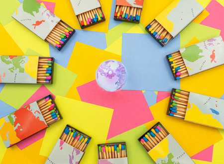 a crystal earth globe surrounded by matchboxes world map with colored sticks on a background of multicolored paper sticky notesの写真素材