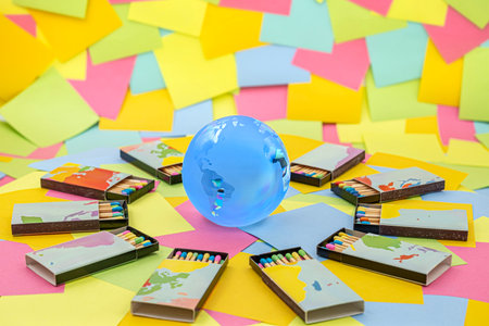 a crystal earth globe surrounded by matchboxes with colored sticks on a background of multicolored...