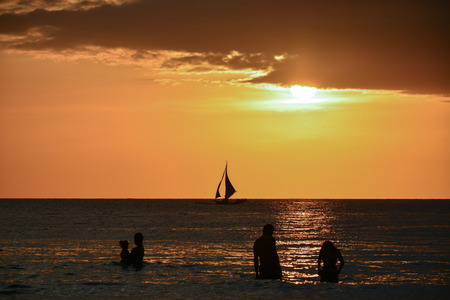 Sunset with people and a boat on the backgroundの写真素材