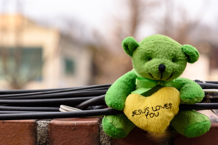 Small green teddy bear leaning on a wall above a yellow heart in his handsの写真素材