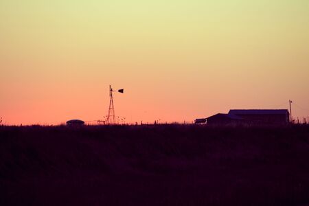 Windmill and a farm silhouette at sunset in Texasの写真素材