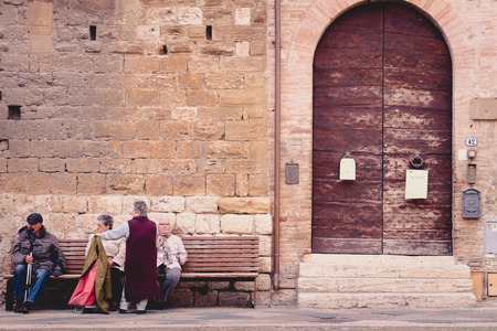 COLLE VAL D'ELSA, ITALY - APRIL 25, 2017 - A group of senior people relax on a public bench in the historic district of Colle Val d'Elsa, a small town near Siena in Tuscanyのeditorial素材