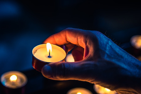 A hand of a man holds a candle in a churchの写真素材