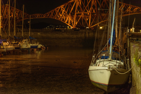 EDINBURGH, SCOTLAND - AUGUST 9, 2017 - Night view of some boats moored at Queens South Ferry, Edinburgh with the Forth Bridge in background.のeditorial素材