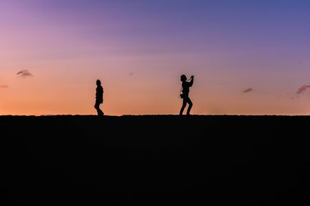 People silhouette against the sky at sunset light on a top of a hill